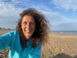 portret van dagcoördinator Anke van Hage, ze heeft een blauwe trui aan en zit aan het strand
